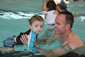 Photo of father holding son smiling while son looks at camera